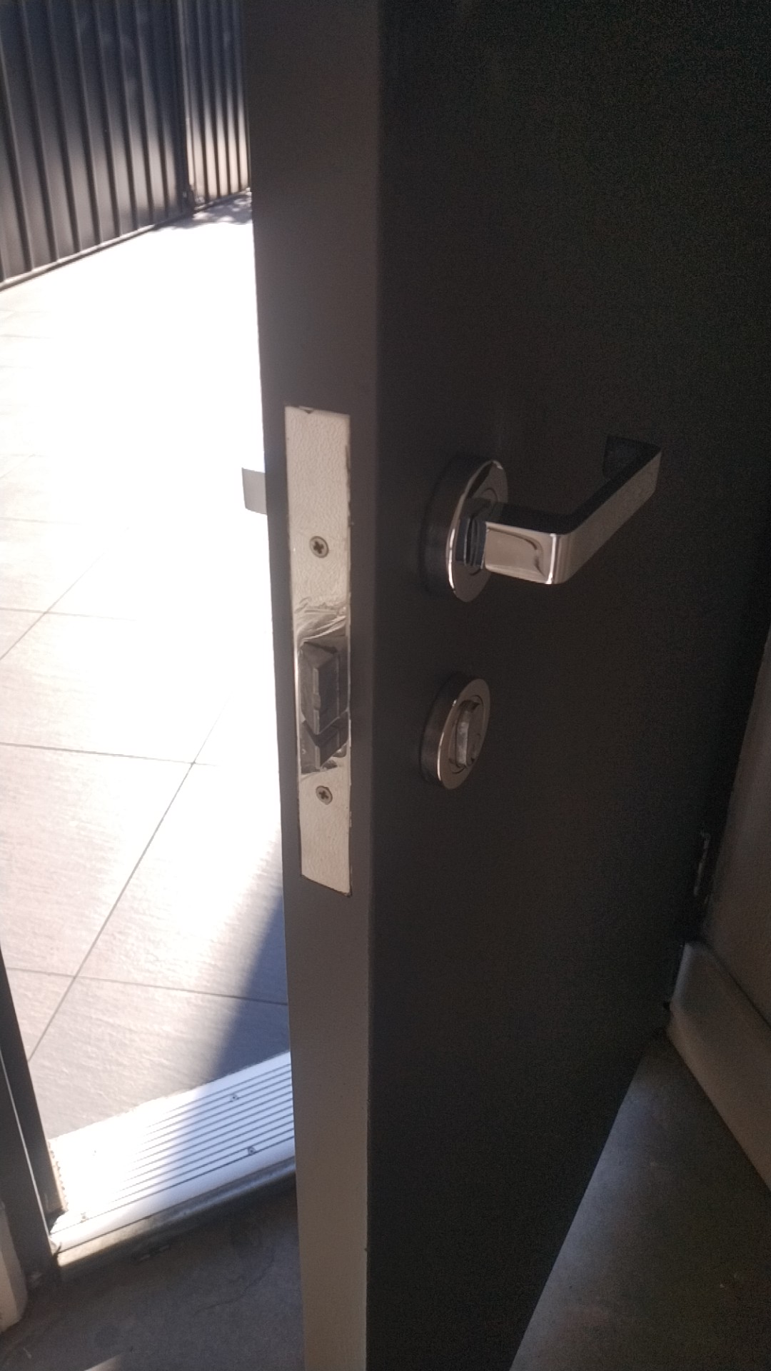 Close up of a fire door edge showing the lever handle, cylinder and the stainless strike plate set into the door